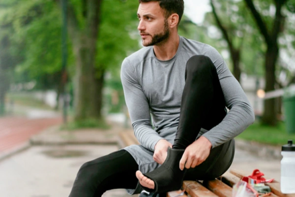 Athlete using hot and cold ankle compression sleeve during outdoor workout recovery