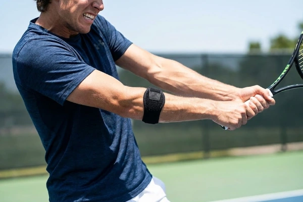 A tennis player wearing a black forearm elbow strap during a powerful swing on the court