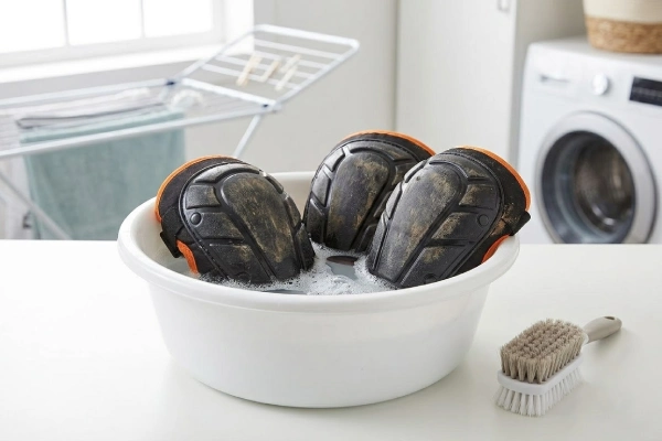 Cleaning dirty work knee pads by hand in a basin with soap
