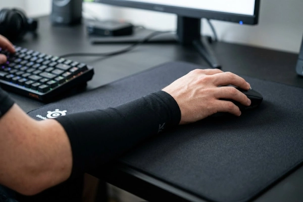 Gamer's arm in a black gaming sleeve using a mouse on a desk