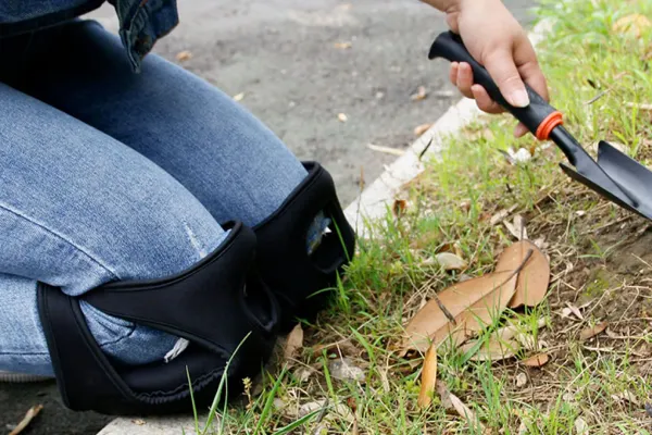 Gardening knee pads worn by a person kneeling on grass while using a trowel