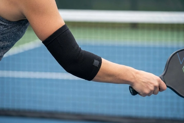 Pickleball elbow compression sleeve worn by a player holding a paddle on the court